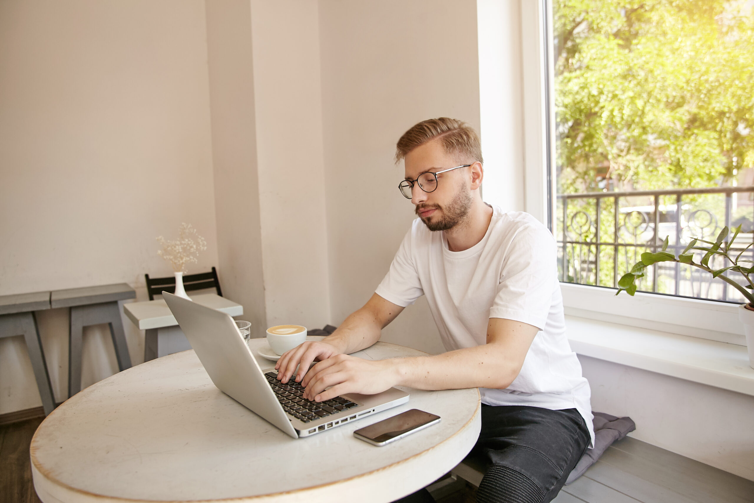 pensive-young-man-working-his-computer-cafe-sitting-table-typing-text-modern-computer-laptop-coffee-smartphone-are-table-remote-work-scaled